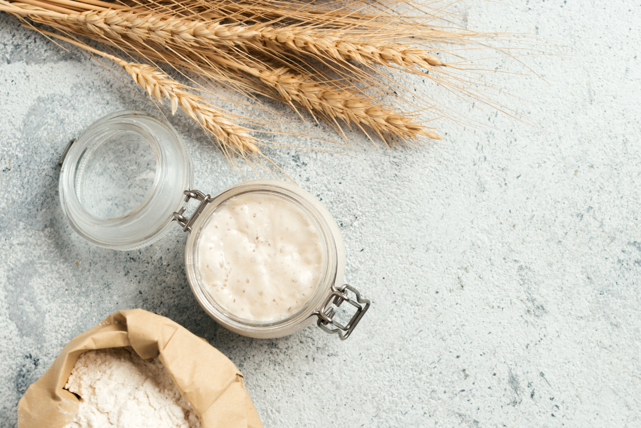 wheat, jar of sourdough starter and a loaf of bread