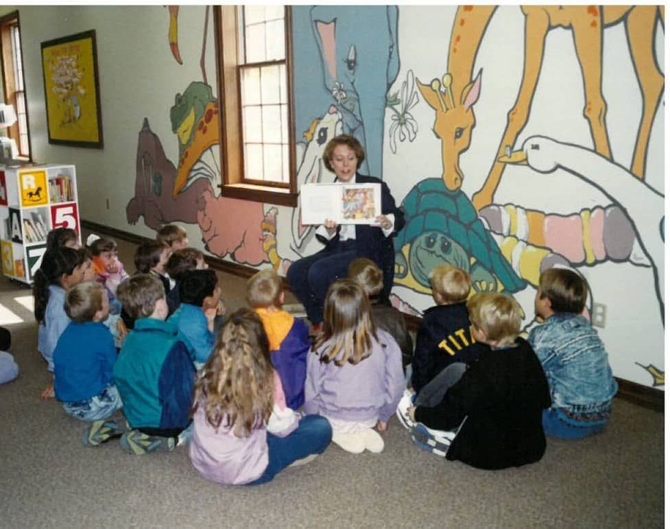 Animal mural painted on the wall of the Children's department librarian is reading a story to children