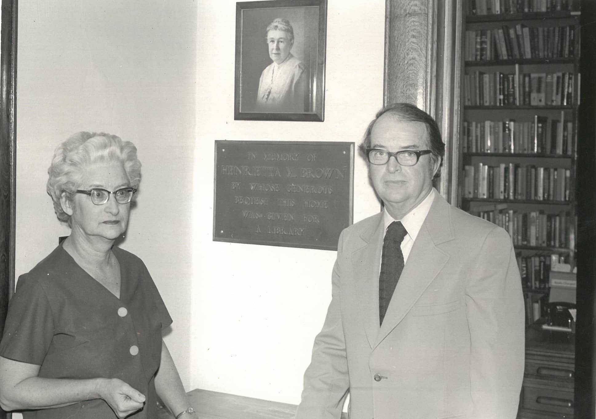 man and woman standing in front of plaque and photograph