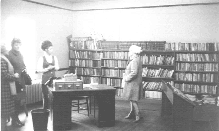 4 women in a library with a desk and book on shelves